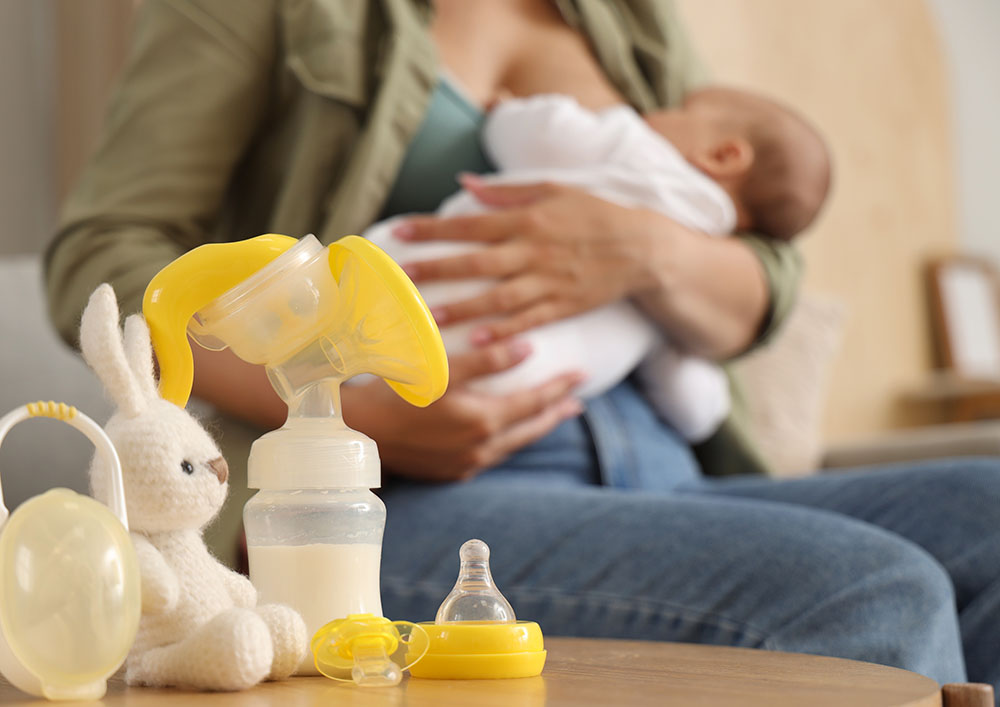 Breast pump with baby pacifier and toy on table in room, closeup