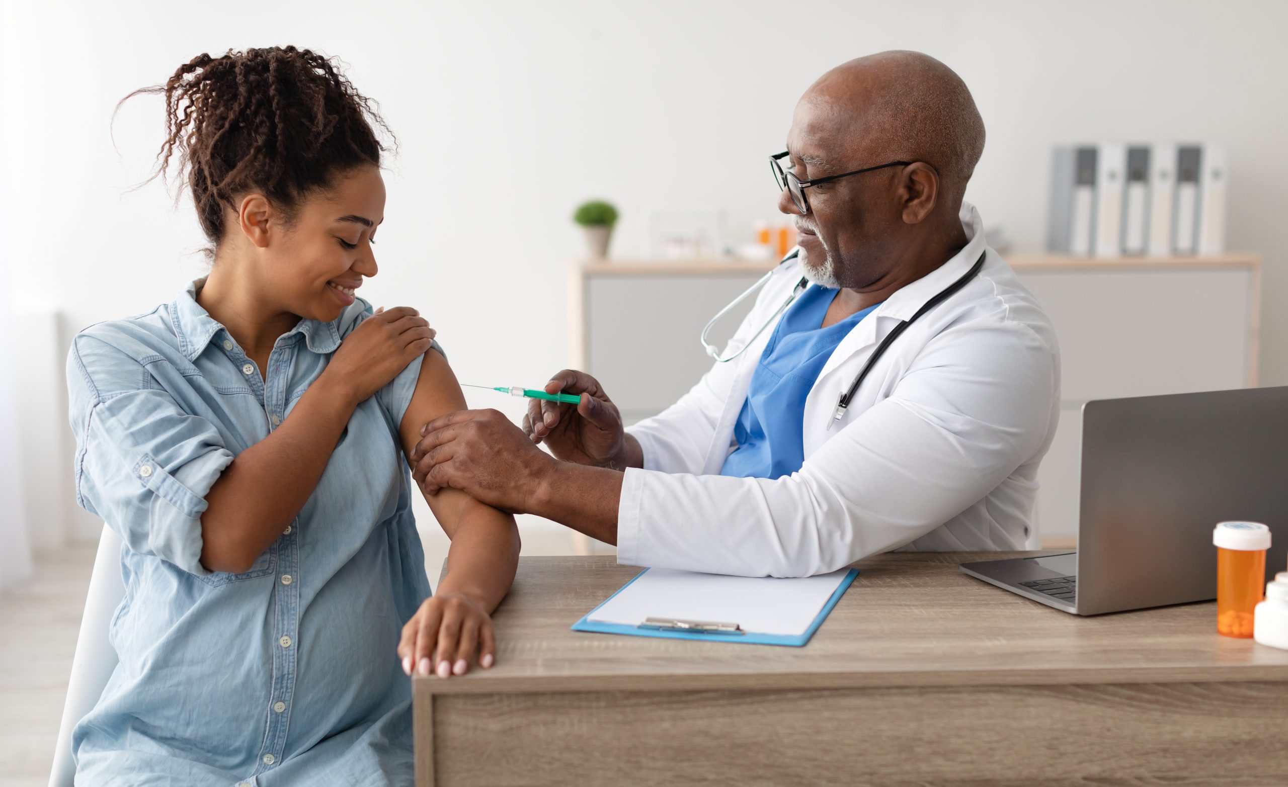 Vaccination In Pregnancy. Smiling Pregnant Young Black Woman Getting Vaccinated At Clinic, Mature Male Doctor In Glasses Giving Vaccine Shot Injecting Mother-To-Be In Arm. Covid-19 And Flu Prevention